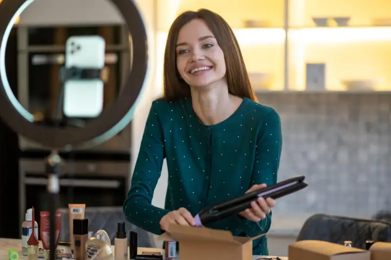 Beauty vlogger unboxes a hair straightener in front of a ring light and phone camera.