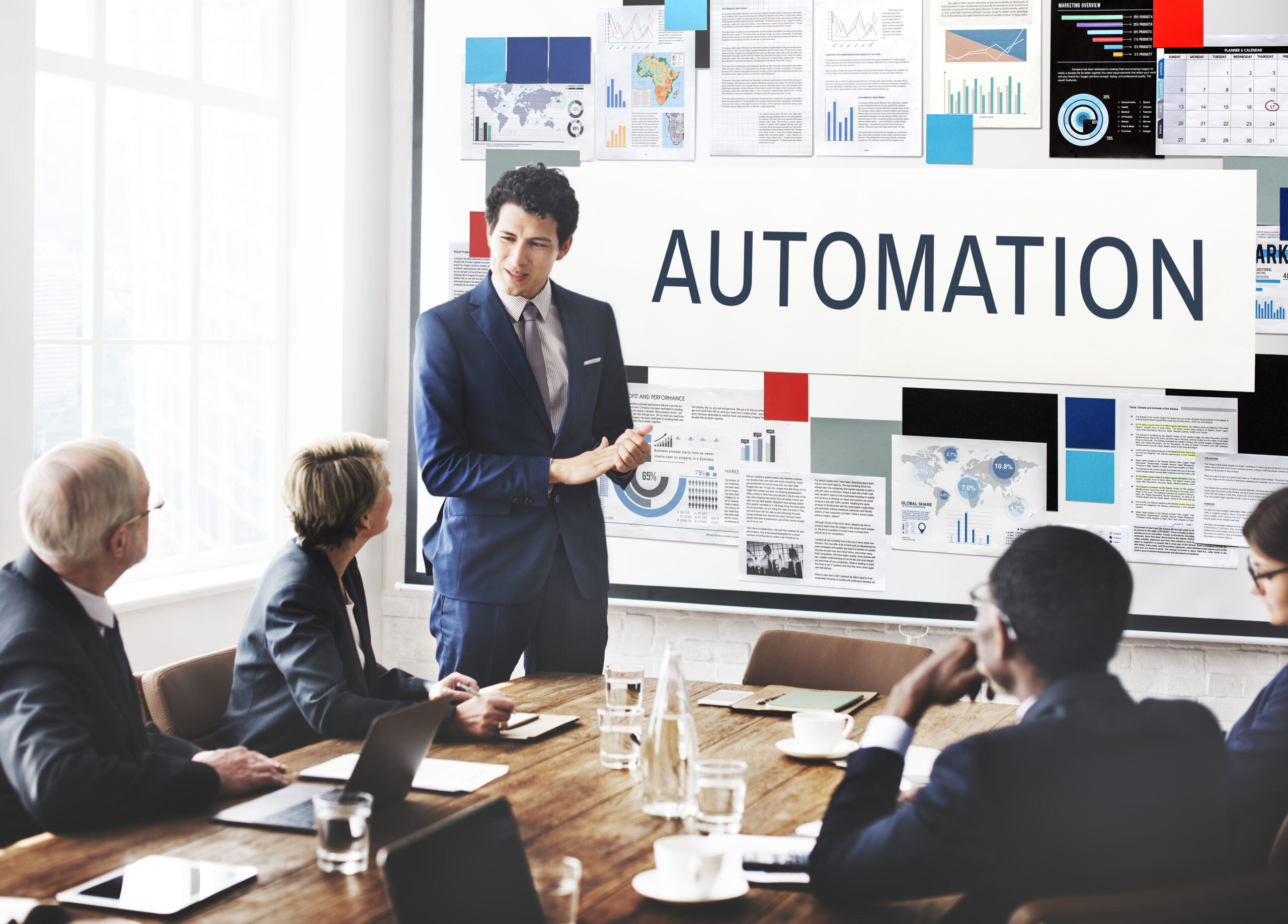 Business professional presents a boardroom slideshow titled “AUTOMATION” to seated executives.