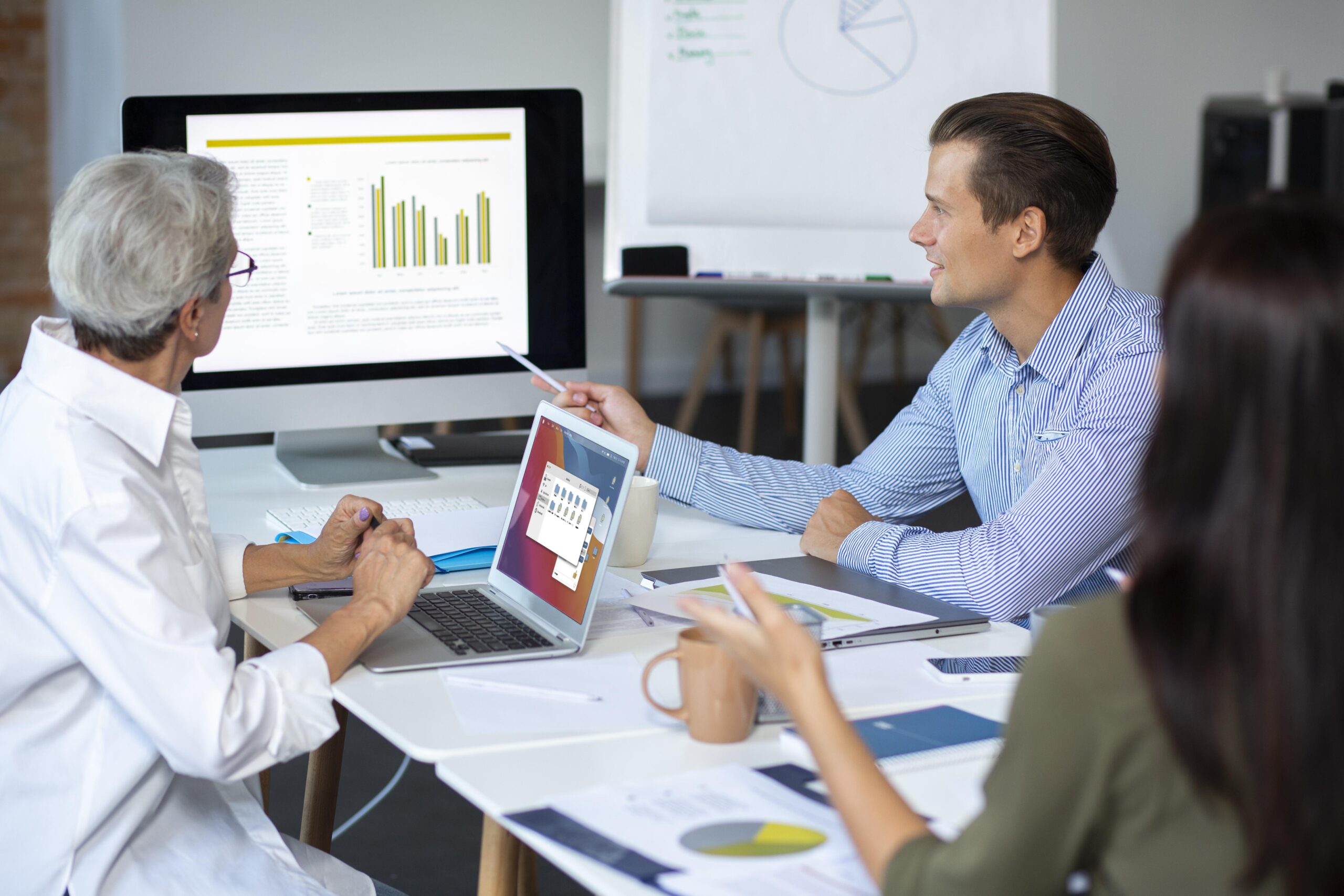 Colleagues in a meeting room examine bar-chart analytics on a large monitor.